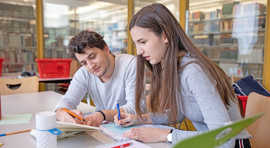 Eine junge Frau und ein junger Mann arbeiten an einem Schreibtisch in einer Bibliothek