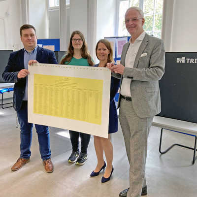 OB Wolfram Leibe, Amtsleiterin Dr. Nicole Thees, Antonia Willger und Thomas Oberkirch vom Bereich Wahlen (von rechts) präsentieren den Stimmzettel für den Stadtrat. Im Hintergrund zu sehen sind die neuen schwarzen Wahlkabinen mit Trier-Logo.