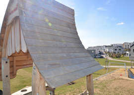 Auf der Spitze des Erdhügels auf dem neuen Filscher Spielplatz steht ein geschwungenes Spielhaus aus Holz.