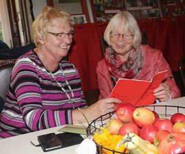 An einem herbstlich gedeckten Tisch informieren sich zwei Besucherinnen in der Programmbroschüre über die Angebote des Trierer Seniorenbüros.