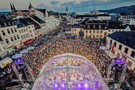 Abendlicher Blick von oben auf eine Open-Air-Bühne in der Fußgängerzone von Trier und ddas Publikum davor