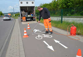 Martin Becker bringt das neue Piktogramm aus Heißplastik mit einem Gasbrenner auf den Geh- und Radweg entlang der Loebstraße auf.